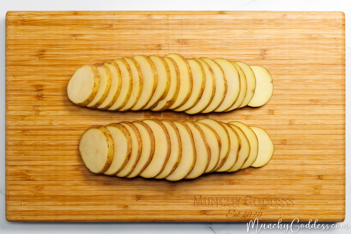 Two russet potatoes each cut into ยผ inch thick rounds on a wood cutting board.