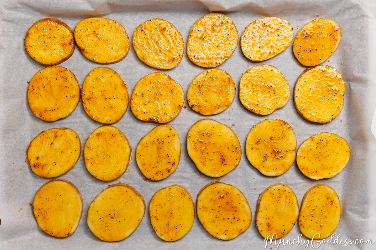 Potato slices coated in an oil seasoning mixture placed on a parchment paper lined sheet pan.
