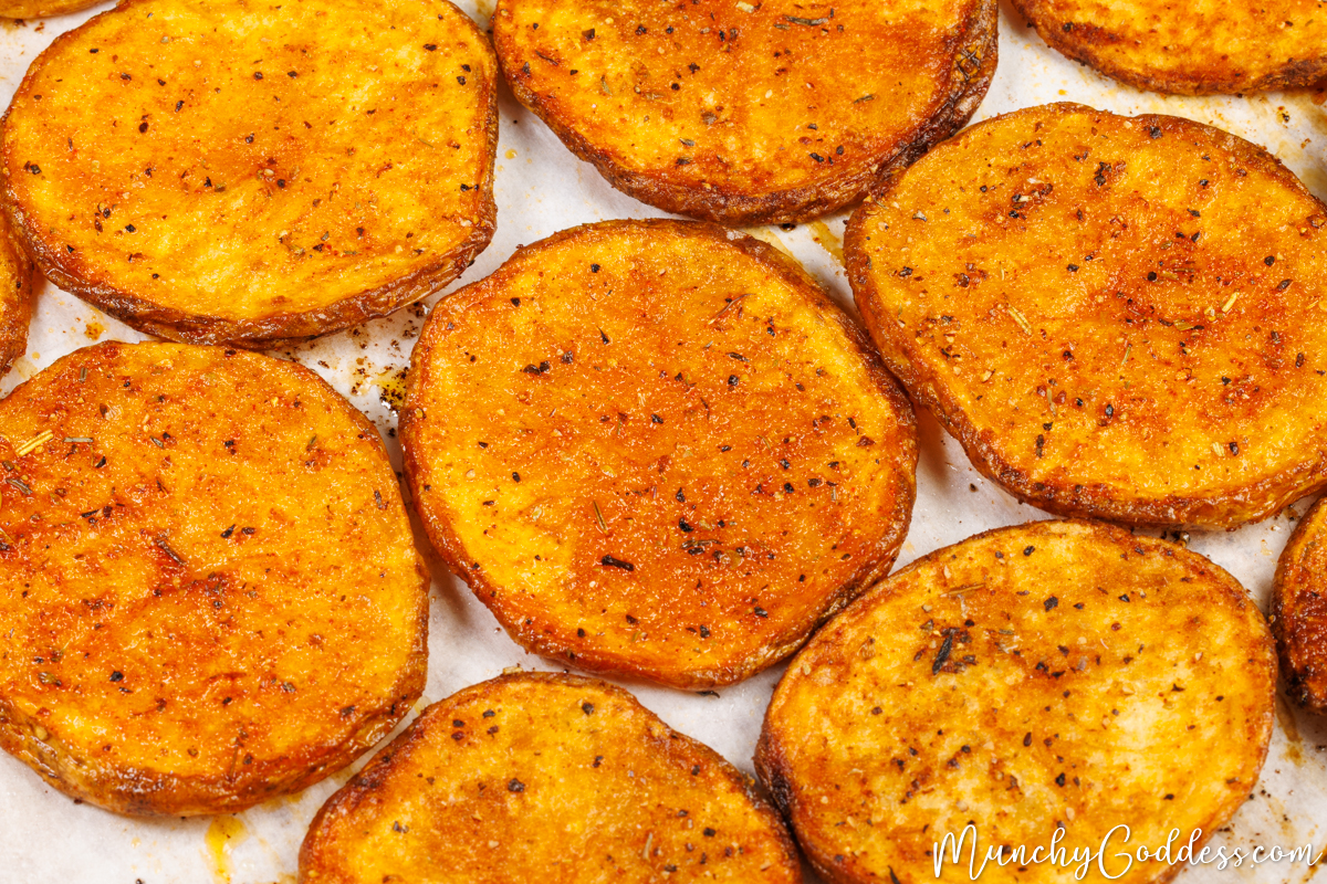 Oven baked potato slices in a single layer on parchment paper.