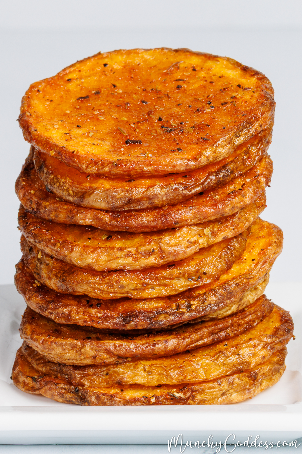 Oven baked potato slices stacked on top of each other showcasing the crispy edges on a white plate.