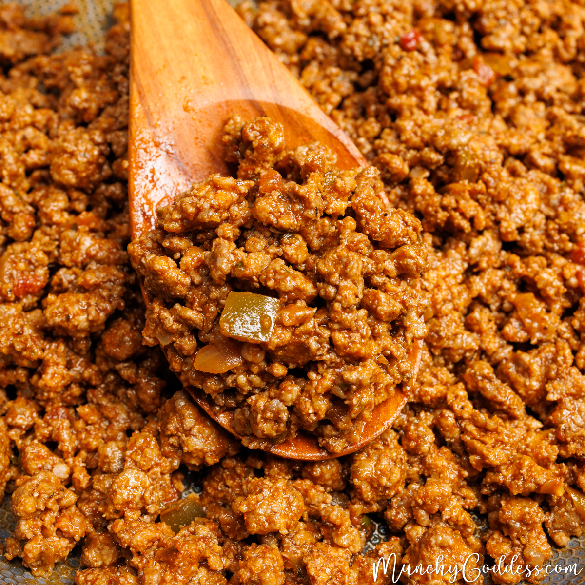 Taco meat on a wooden spoon sitting on top of more taco meat.