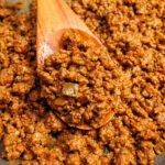 Taco meat on a wooden spoon sitting on top of more taco meat.