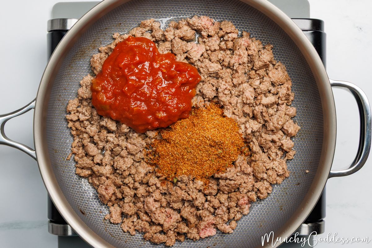Taco seasoning and chunky salsa on top of browned ground beef and water in a pan.