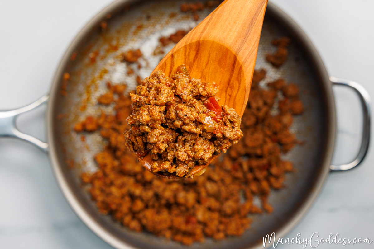 Taco meat being lifted up by a wooden spoon out of a pan.