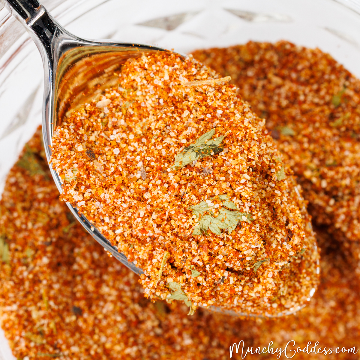 Taco seasoning being lifted up by a spoon from a glass jar filled with taco seasoning.