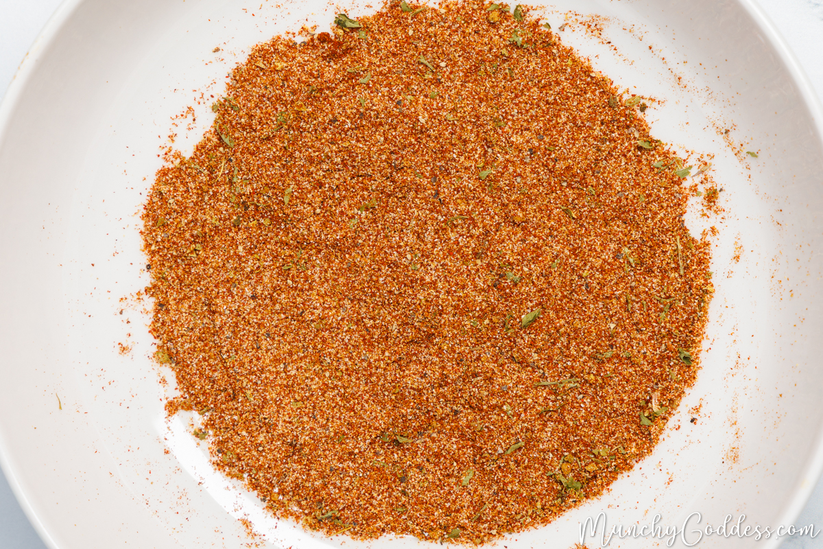 Smoked paprika, ground cumin, garlic powder, onion powder, dried oregano, salt, chili powder, parsley flakes, and ground black pepper blended in a white bowl.