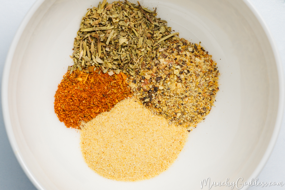 Cajun seasoning, Italian seasoning, lemon pepper seasoning, and garlic powder neatly placed next to each other in an off white bowl.
