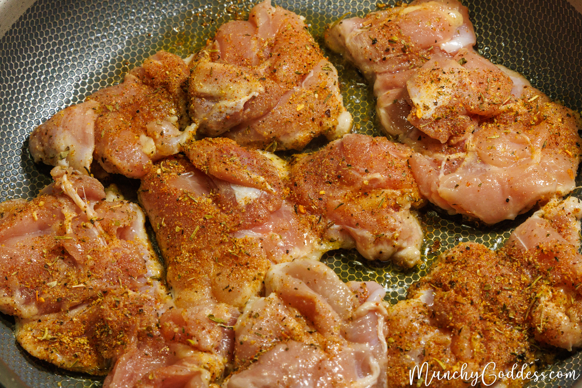 Cajun seasoned chicken thighs placed smooth side down in a heated skillet with olive oil.