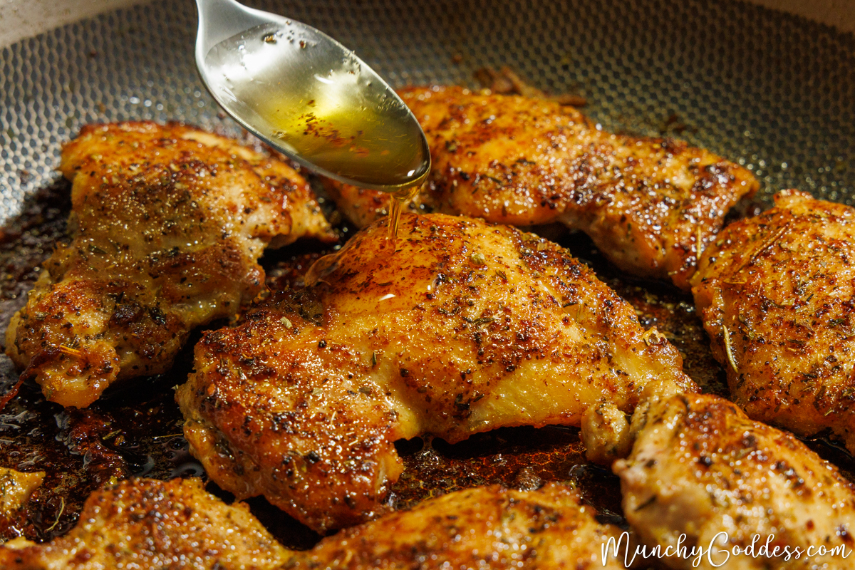 A spoon drizzling butter sauce on top of a cooked Cajun butter chicken thigh inside a skillet.