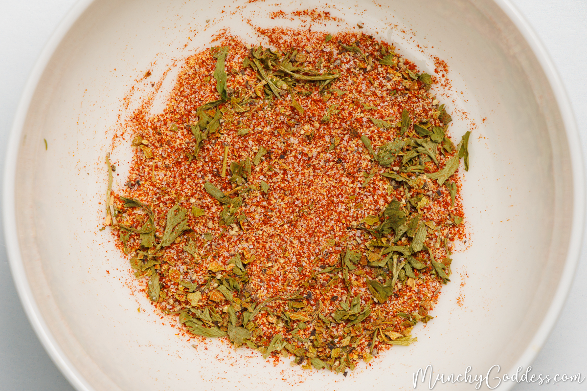 Dried oregano, parsley flakes, smoked paprika, salt, ground black pepper, and garlic powder blended in an off white bowl.