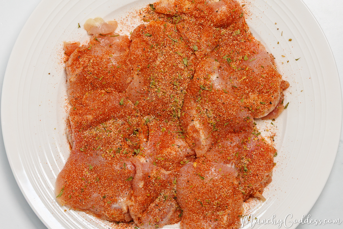 Seasoned boneless skinless chicken thighs on an off white plate.