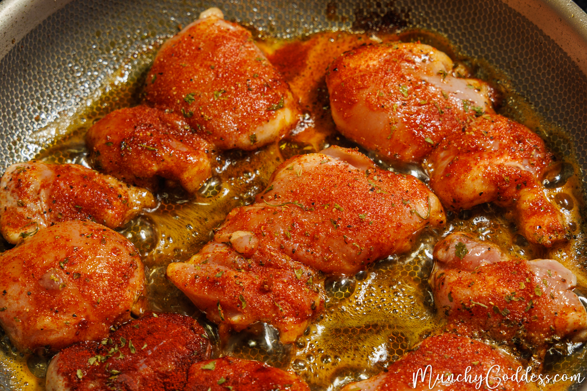 Seasoned boneless skinless chicken thighs placed smooth side up in a heated skillet containing melted butter and olive oil.