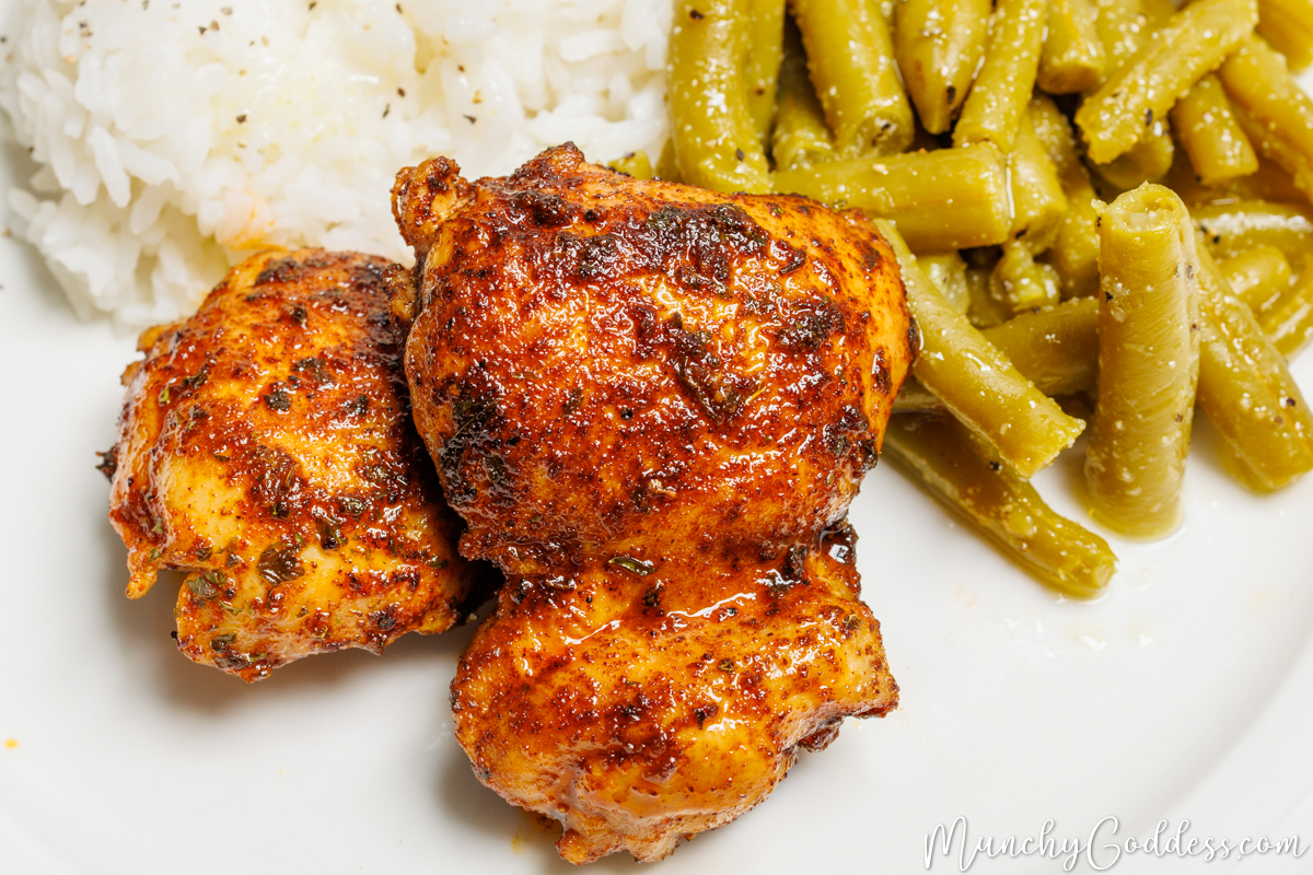 Pan seared chicken thighs on a white plate with rice and green beans.
