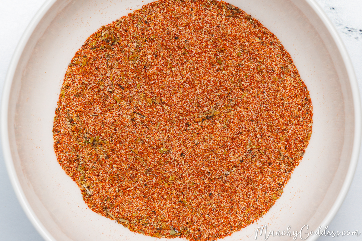 Smoked paprika, salt, onion powder, dried thyme, cayenne pepper, ground black pepper, dried oregano, and garlic powder blended in an off-white bowl.