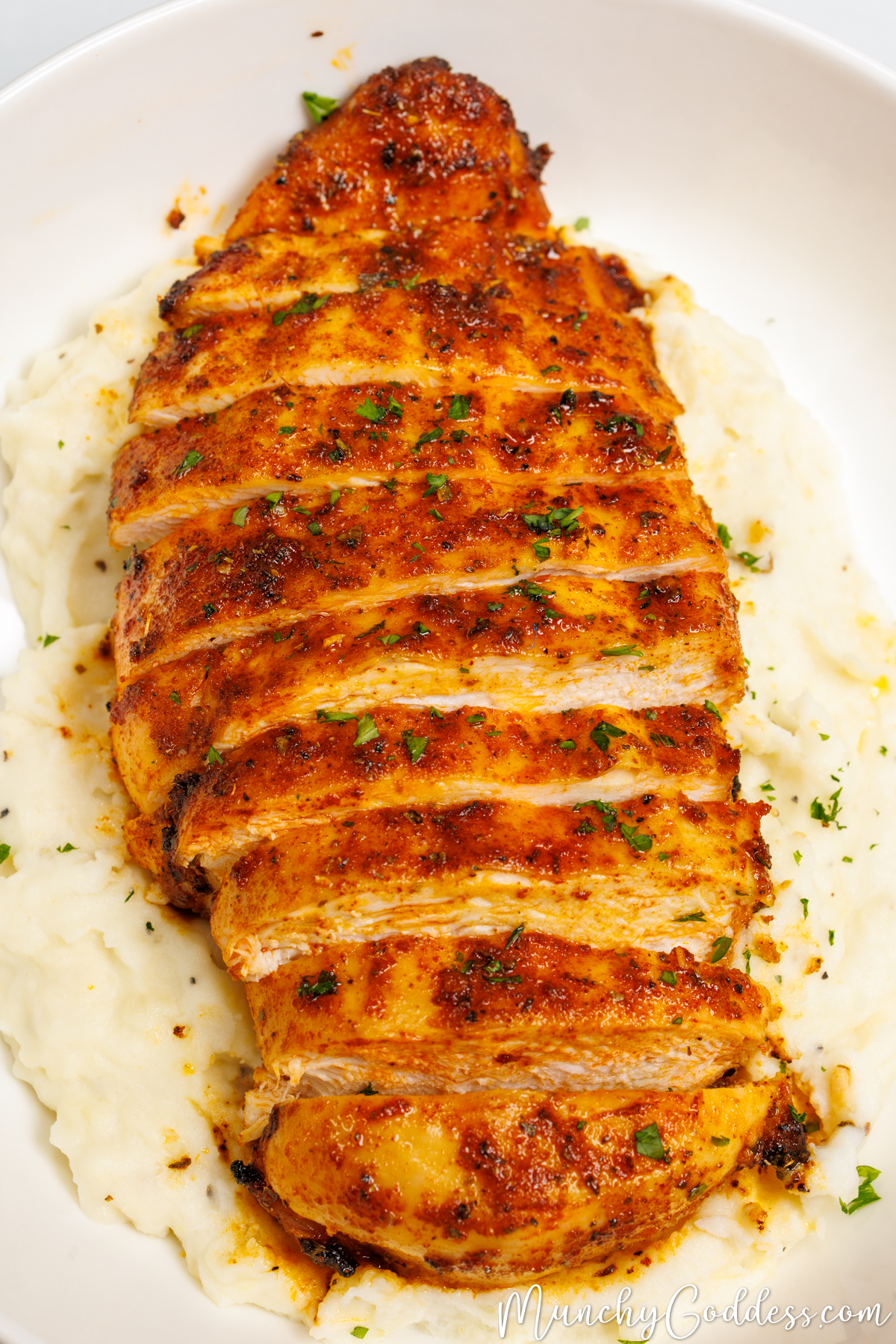 Sliced juicy air fryer chicken breast topped with freshly chopped parsley on a bed of mashed potatoes in an off-white bowl.