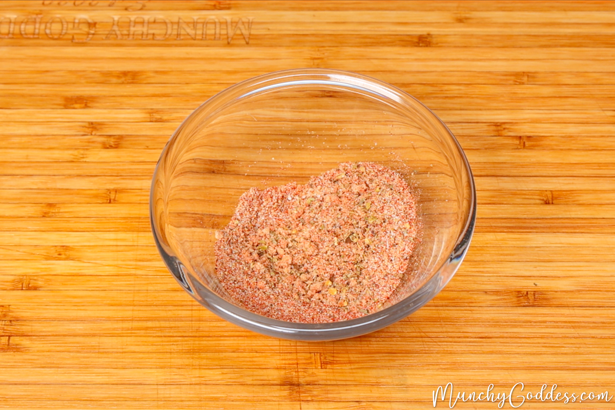 Brown sugar, smoked paprika, Italian seasoning, garlic powder, onion powder, salt, and ground black pepper blended in a small glass bowl on a wood cutting board.