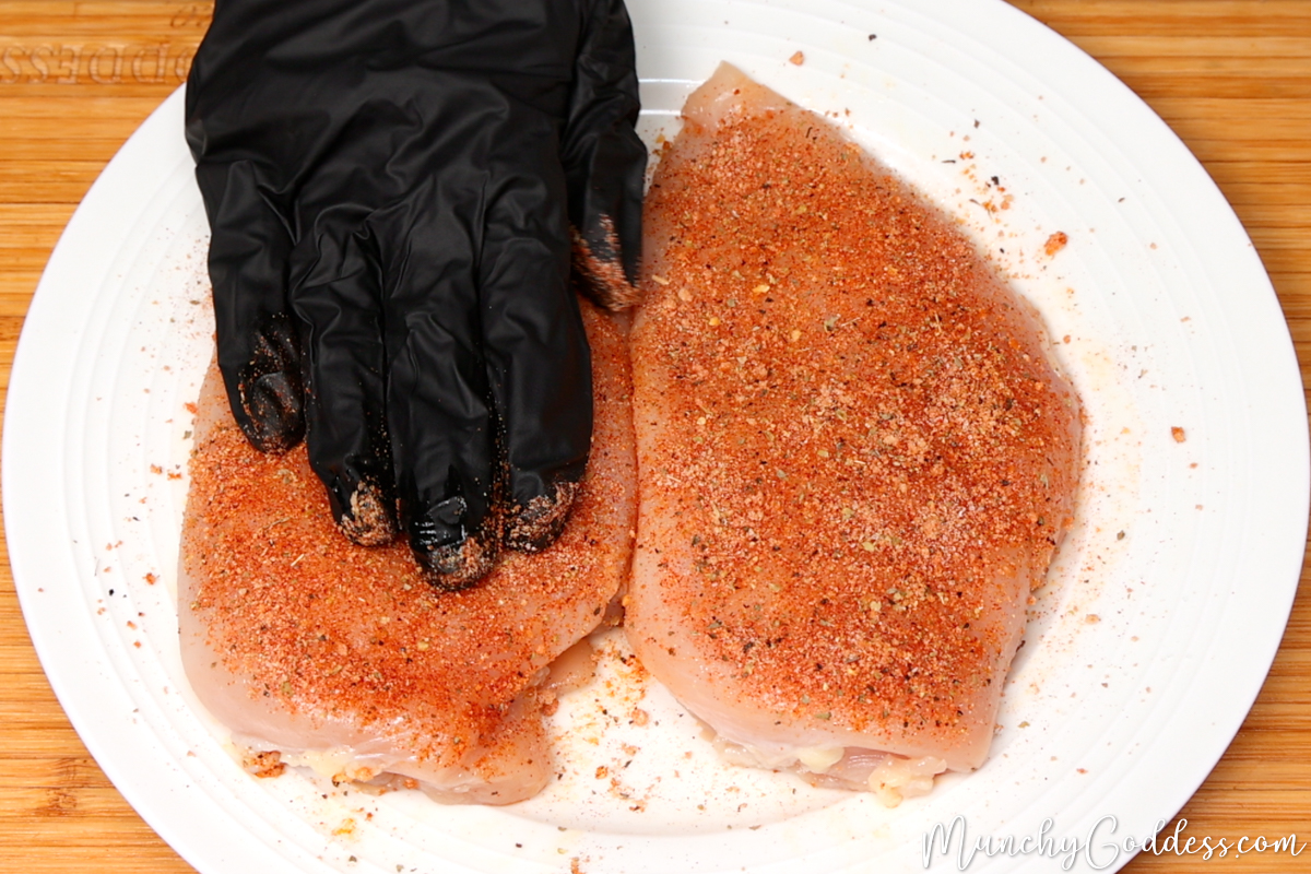 Seasoning being rubbed onto a chicken breast on an off-white plate.
