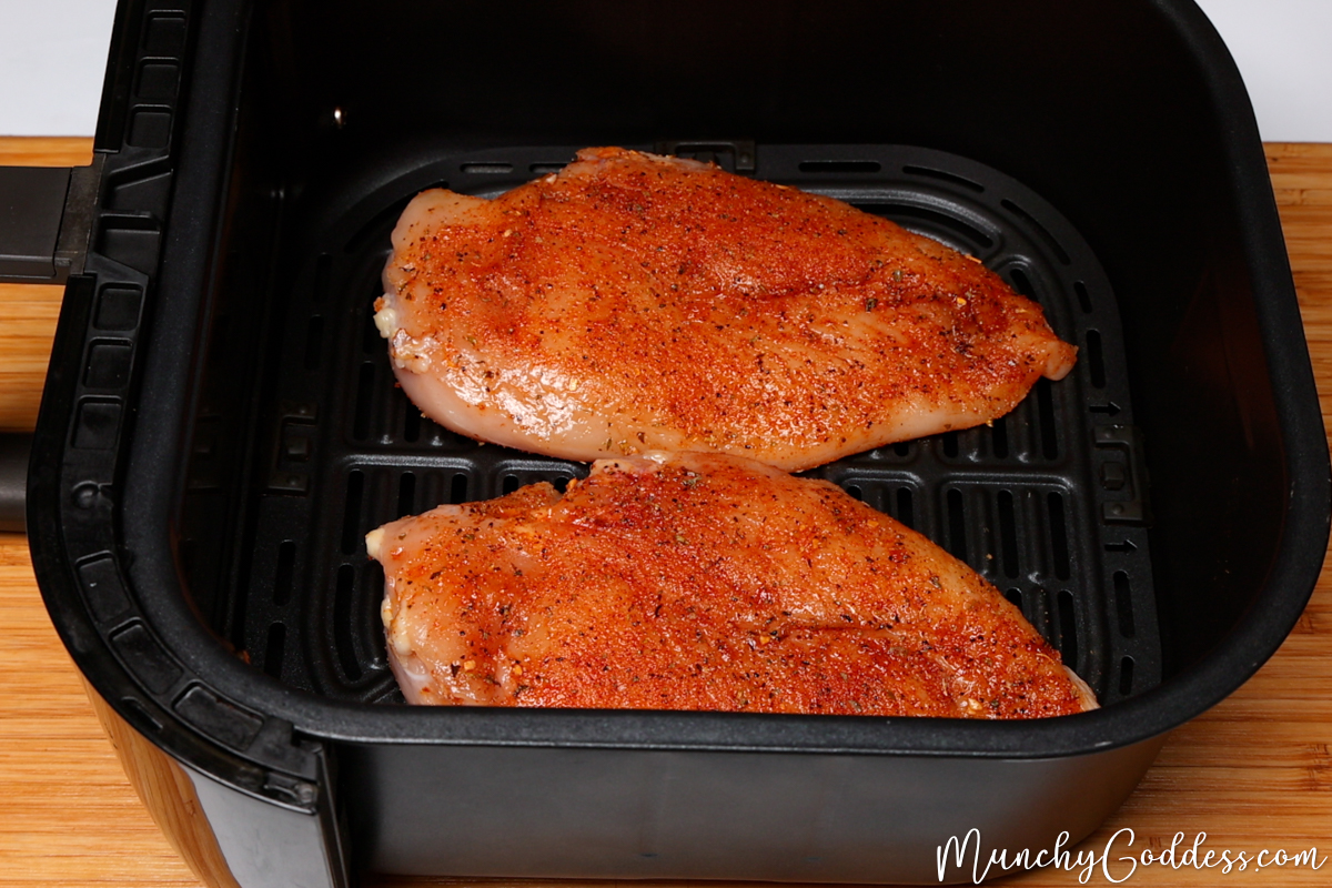 Seasoned raw chicken breast added to a preheated black air fryer basket smooth side down.