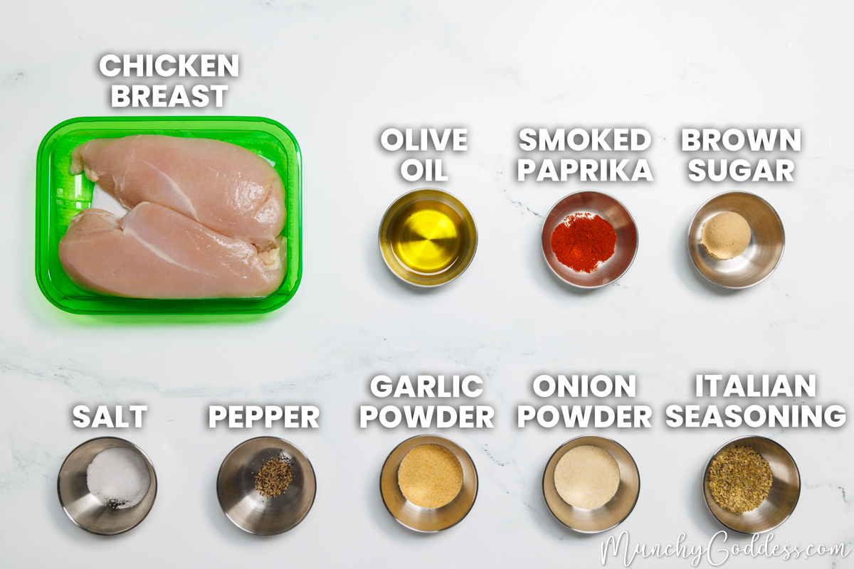 Air Fryer Chicken Breast recipe ingredients in various dishes on a white marble surface: chicken breast, olive oil, smoked paprika, brown sugar, salt, ground black pepper, garlic powder, onion powder, and Italian seasoning.