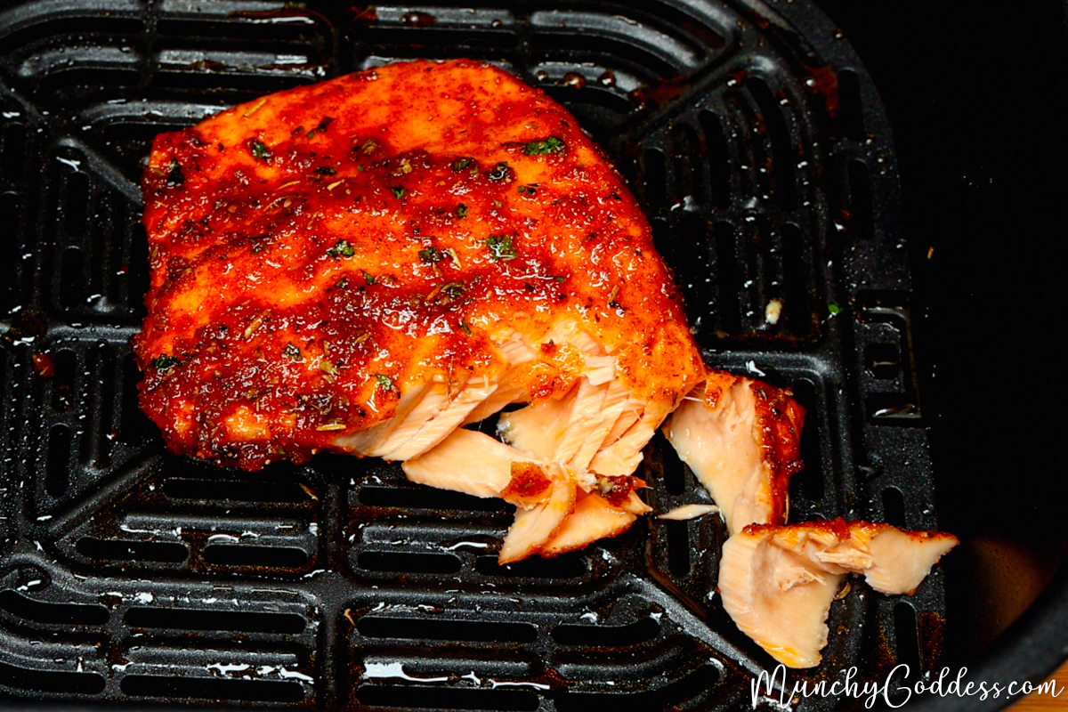 Air fryer salmon in a black air fryer basket forked open showing the perfectly cooked flaky inside.