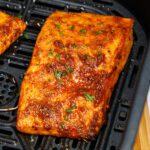 Perfectly seasoned and cooked salmon topped with fresh parsley on a black air fryer tray.