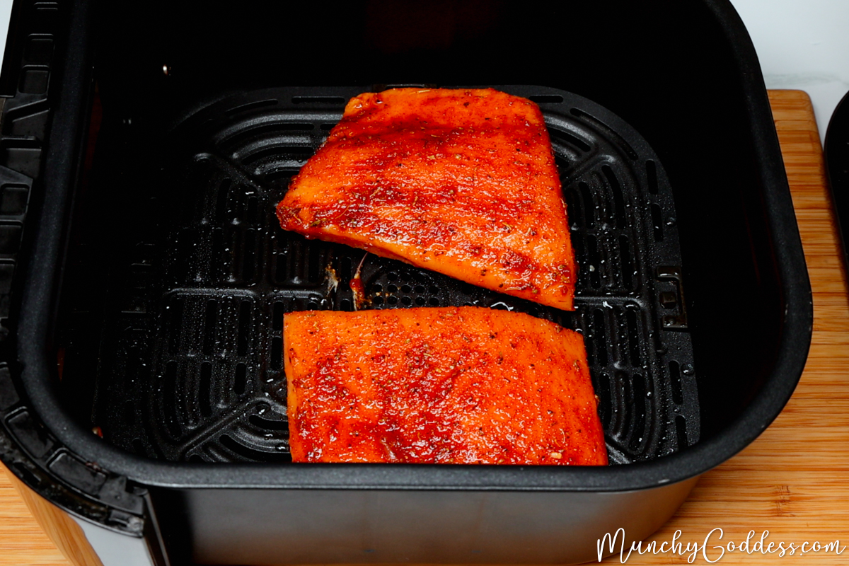 Seasoned salmon fillets in a black air fryer basket ready to be cooked.