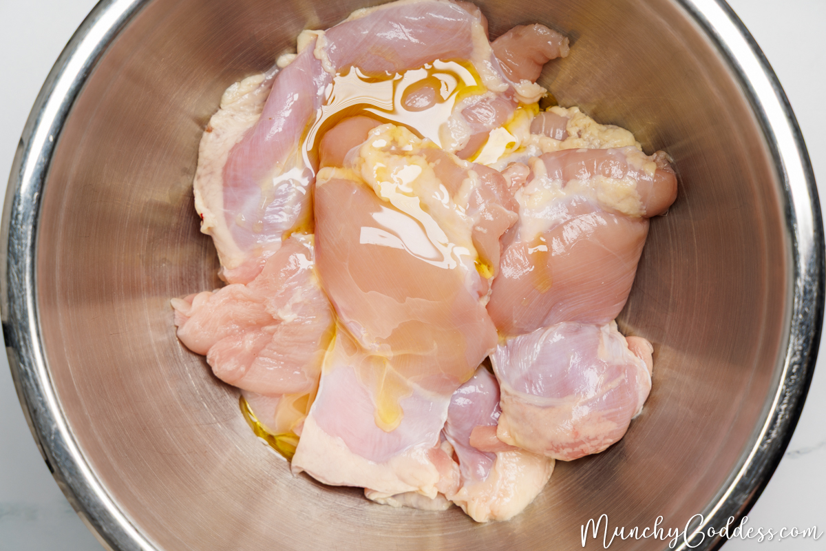 boneless skinless chicken thighs drizzled with olive oil in a silver mixing bowl.