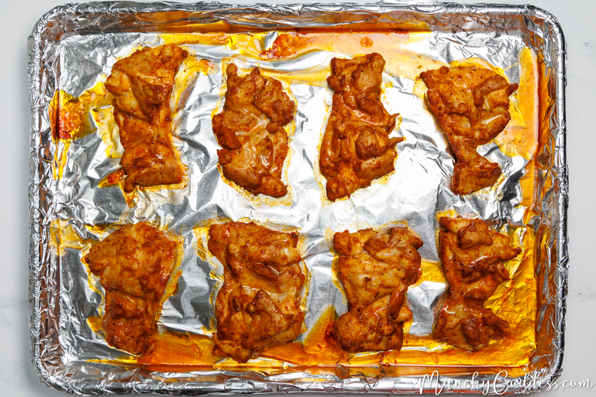 Boneless skinless chicken thighs after being baked for 20 minutes smooth side down on a sheet pan lined with foil.