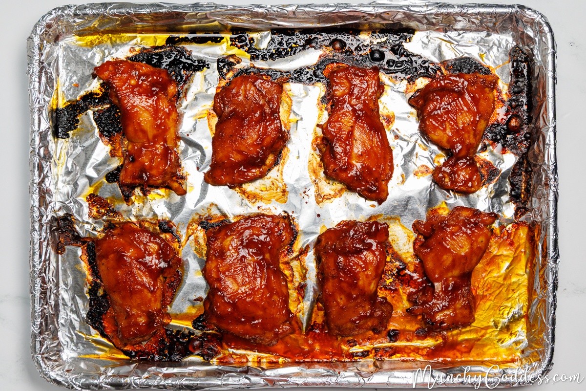 Baked BBQ chicken thighs smooth side up on a sheet pan lined with foil.