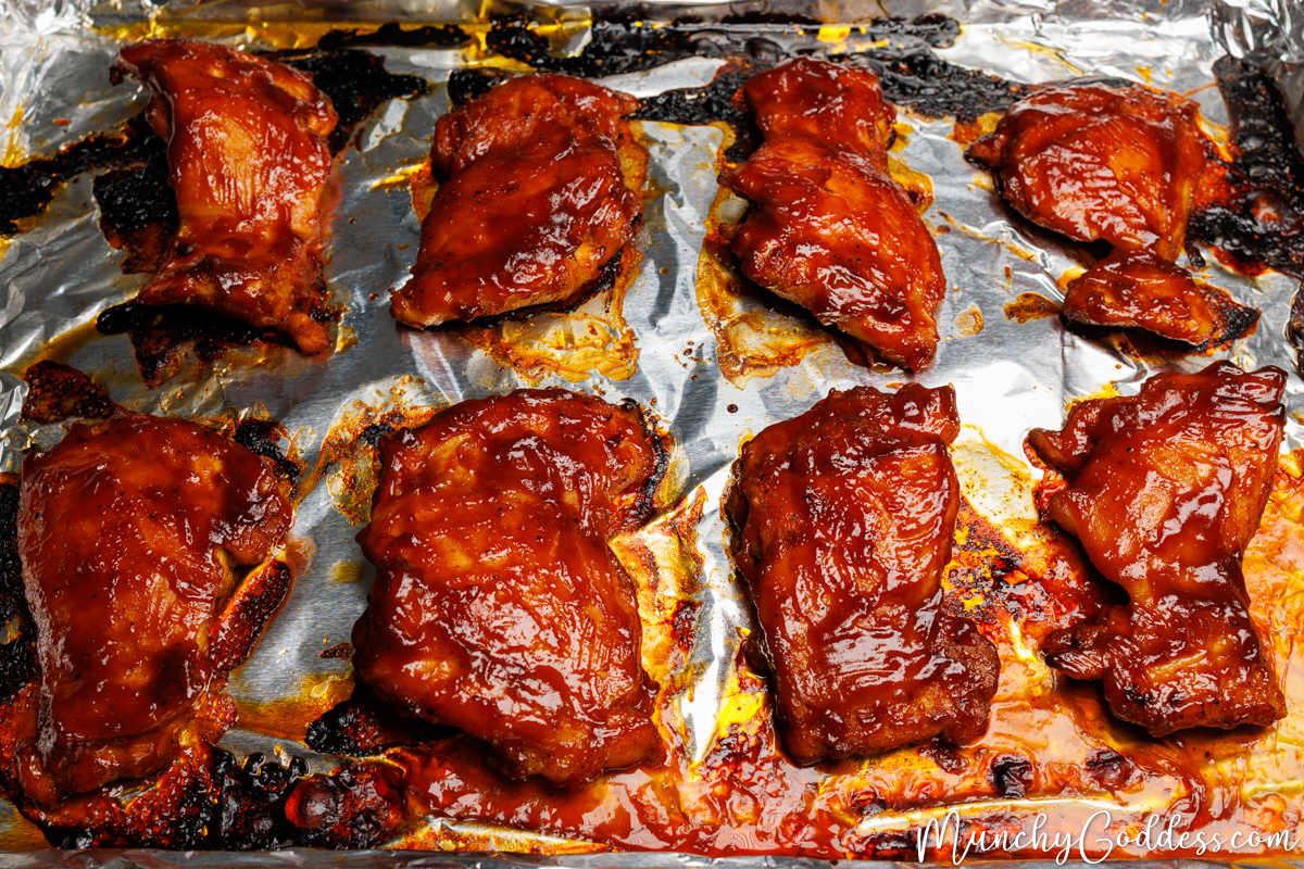 Baked BBQ chicken thighs smooth side up with extra crispy edges on a sheet pan lined with foil.