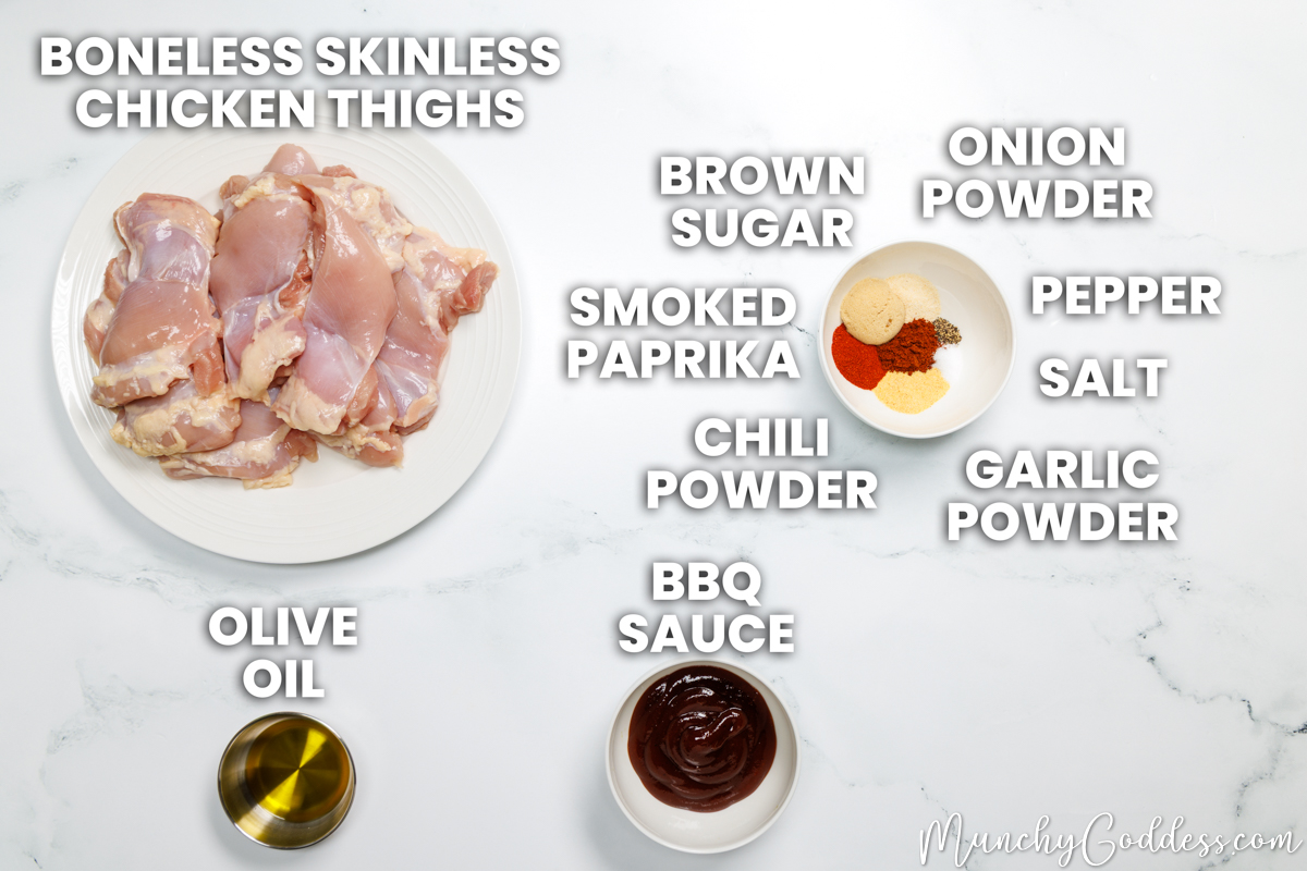 Baked BBQ chicken thighs recipe ingredients in various dishes on a white marble surface: boneless skinless chicken thighs, olive oil, BBQ sauce, brown sugar, onion powder, ground black pepper, salt, garlic powder, chili powder, and smoked paprika.