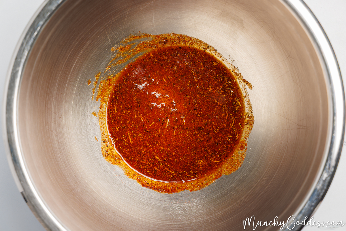 Olive oil, Italian seasoning, smoked paprika, salt, ground black pepper, garlic powder, and onion powder blended together to make an olive oil seasoning mixture in a silver mixing bowl.