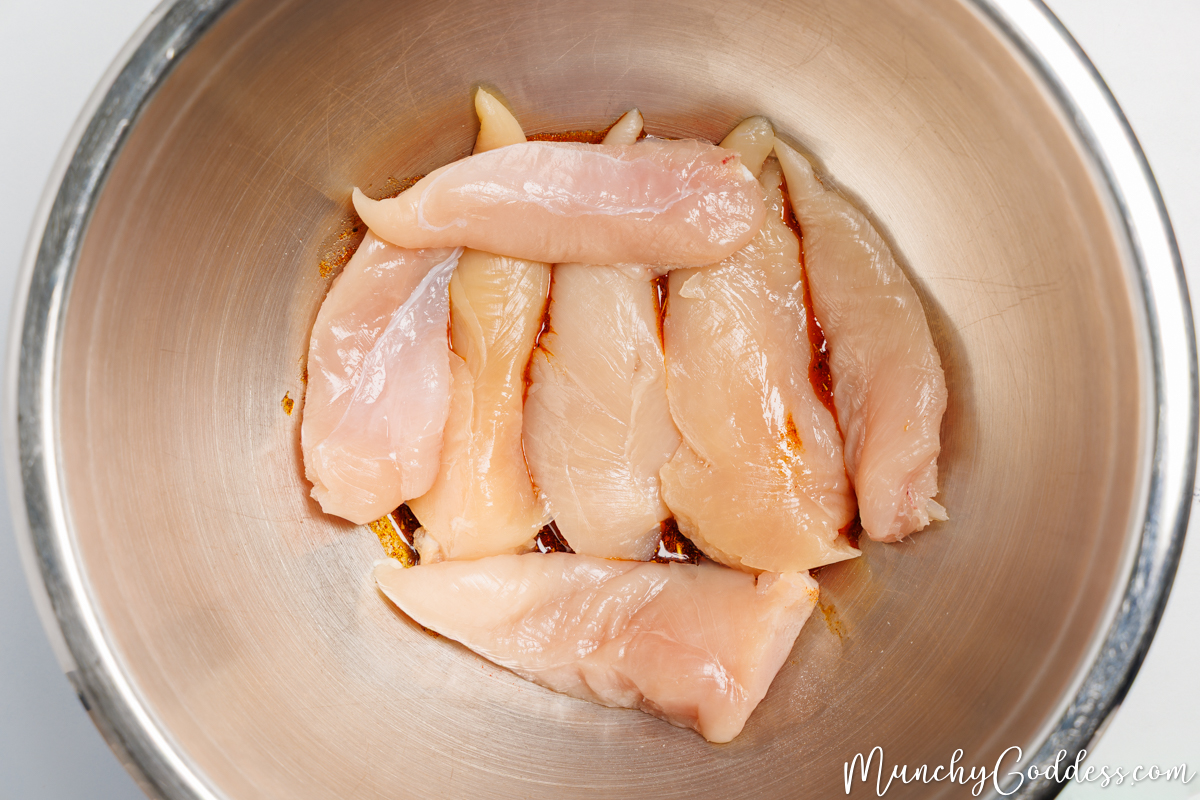 Chicken tenderloins added to a silver mixing bowl containing an olive oil seasoning mixture.