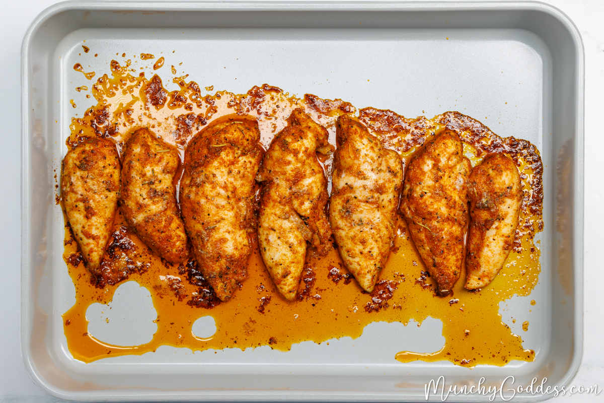 Chicken tenderloins perfectly seasoned and baked in a single layer in a light gray baking dish.