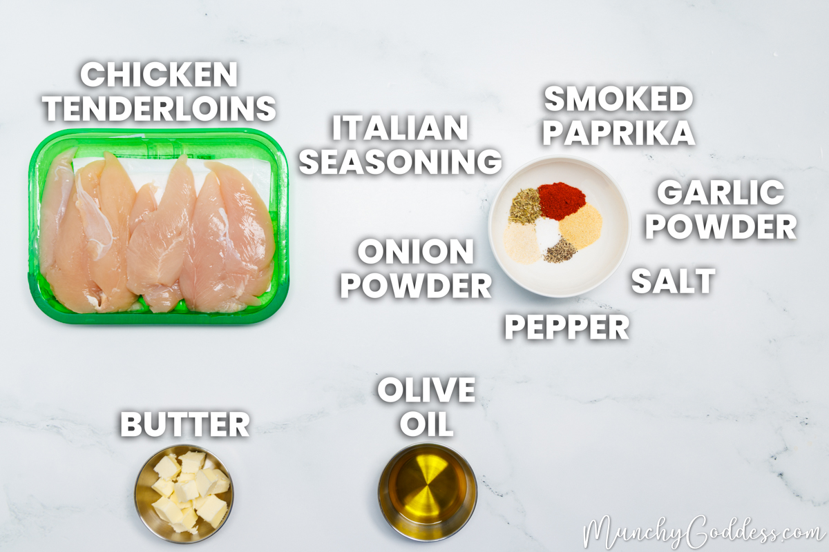 Baked chicken tenderloins recipe ingredients in various dishes on a white marble surface: chicken tenderloins, butter, olive oil, Italian seasoning, smoked paprika, garlic powder, salt, ground black pepper, and onion powder.
