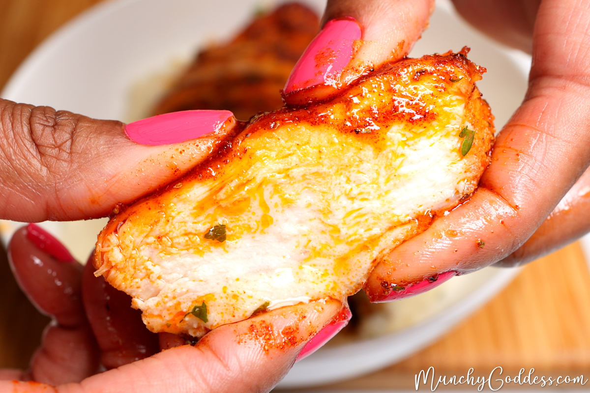 A slice of air fried chicken breast being squeezed on the top and bottom to demonstrate the juiciness of the of the perfectly cooked meat.