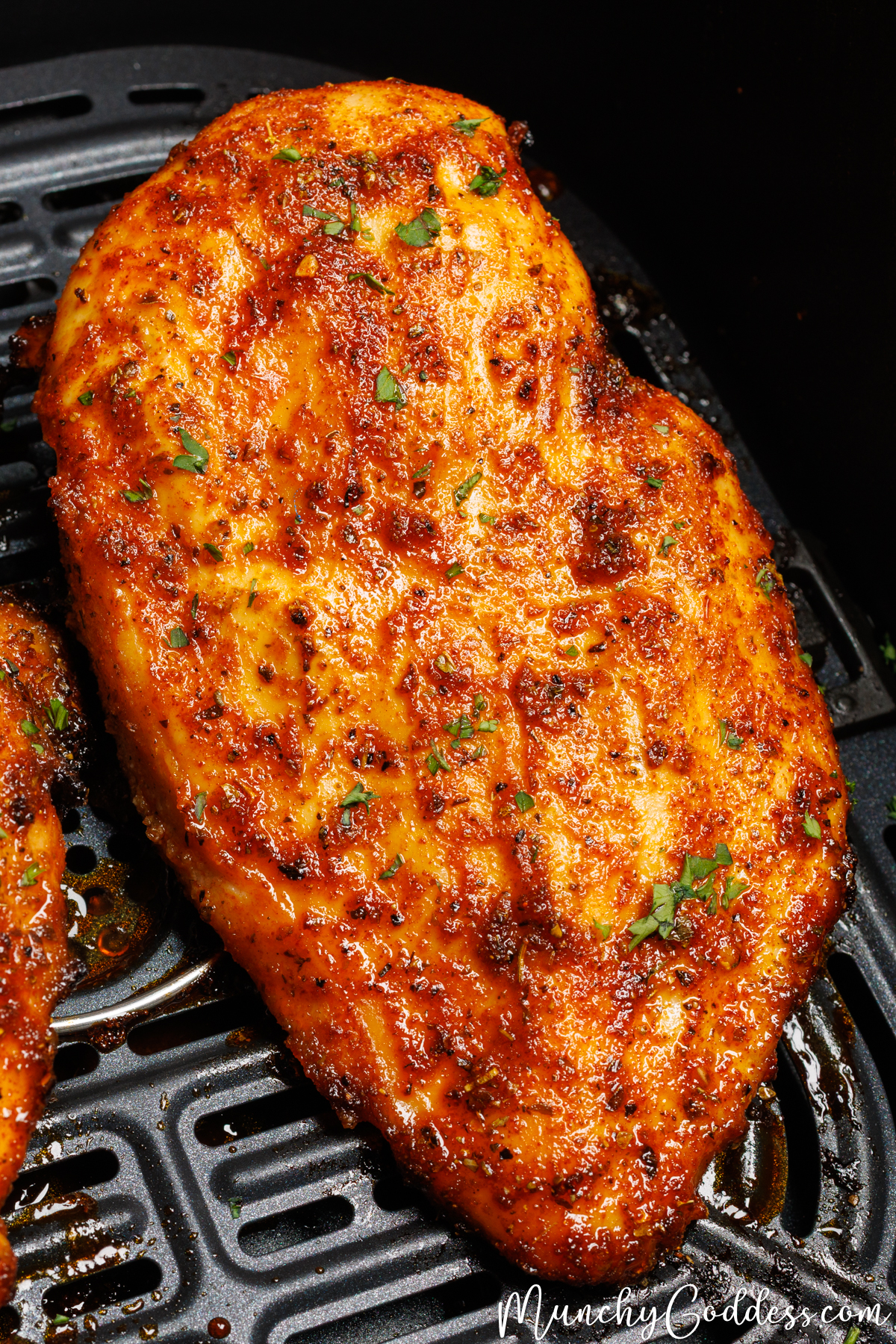 Perfectly seasoned and cooked chicken breast topped with fresh chopped parsley in a black air fryer basket.