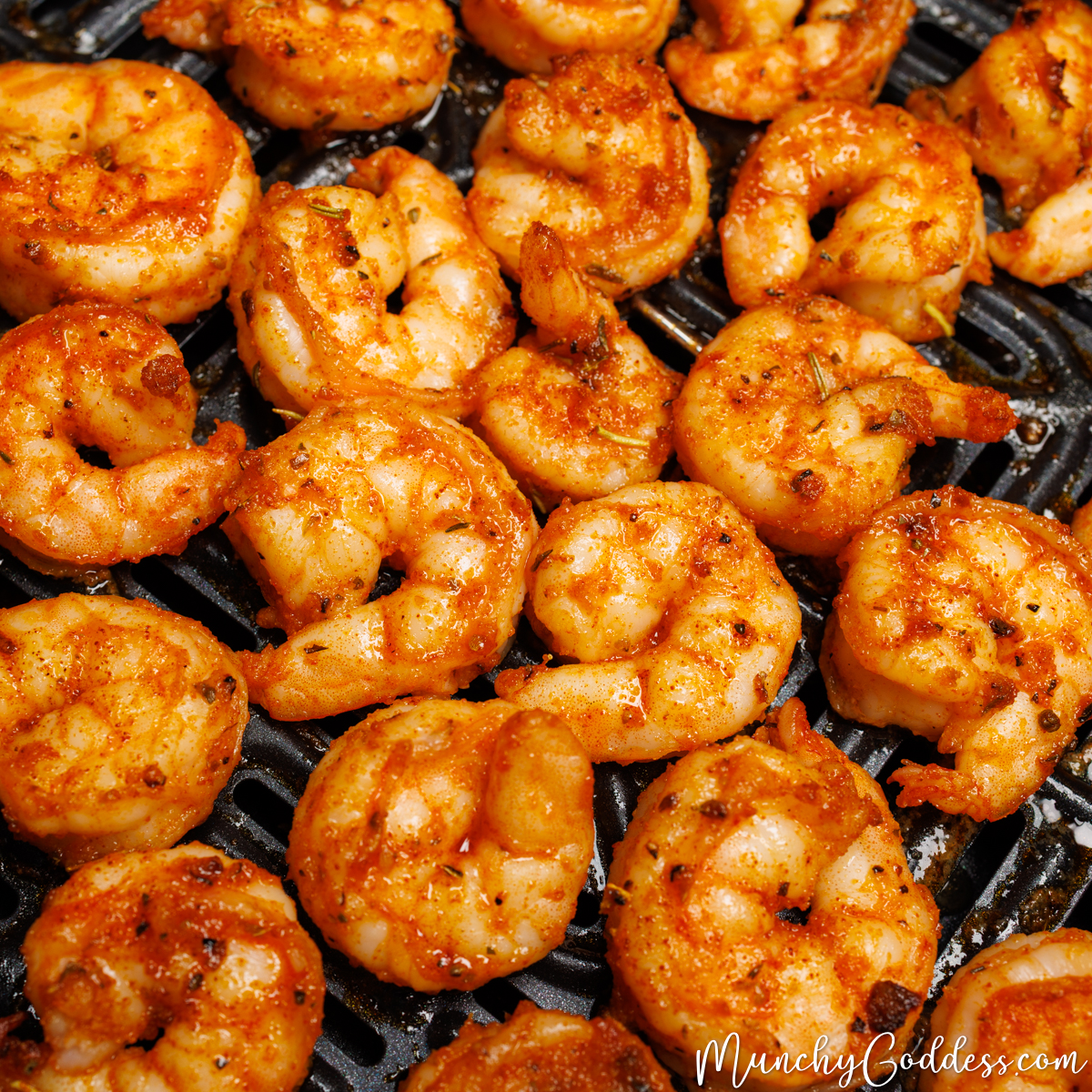 Seasoned air fryer shrimp on a black air fryer tray.