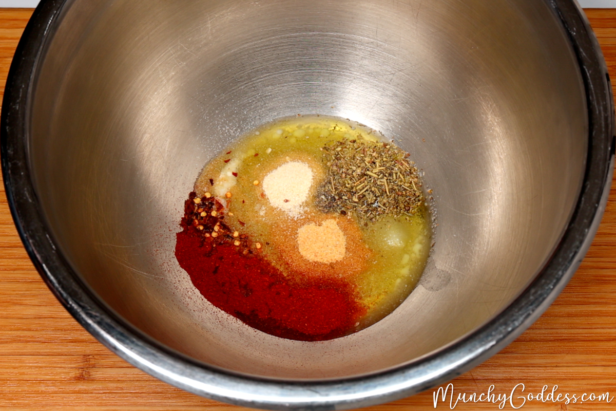 Melted butter, olive oil, salt, ground black pepper, onion powder, garlic powder, Italian seasoning, smoked paprika, and red pepper flakes neatly placed in a silver mixing bowl.