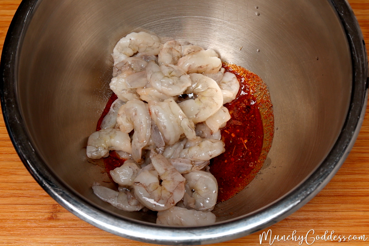 Raw jumbo shrimp added to a silver mixing bowl with a melted butter and olive oil seasoning mixture.