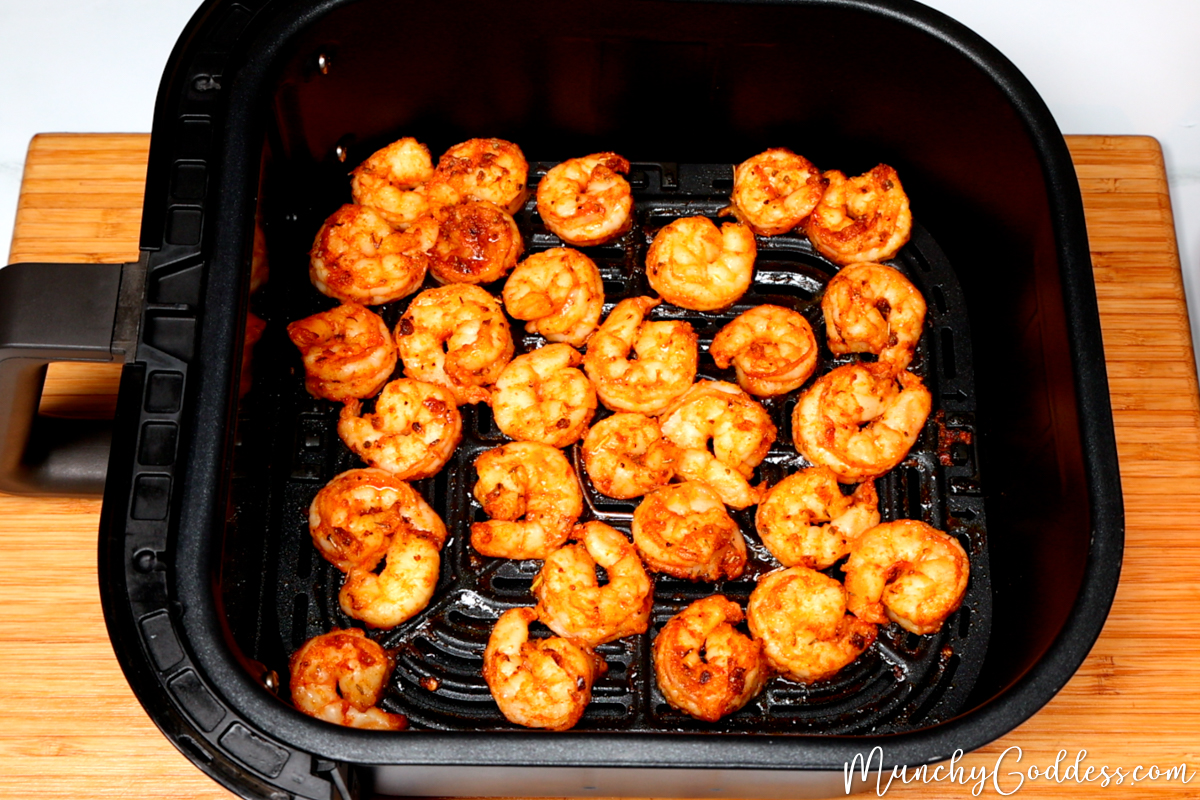 Fully cooked shrimp in a black air fryer basket on a wood cutting board.