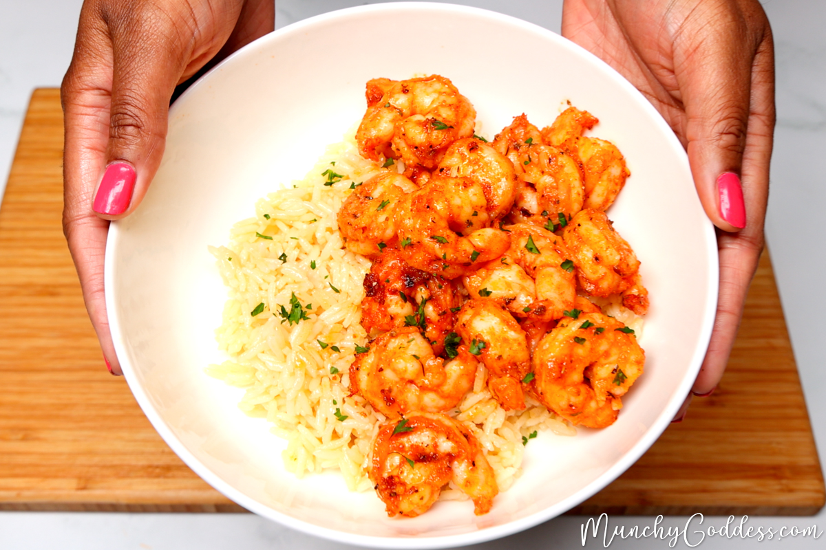 Air fryer shrimp on a bed of rice topped with fresh chopped parsley in an off-white bowl being lifted in the air with hands.
