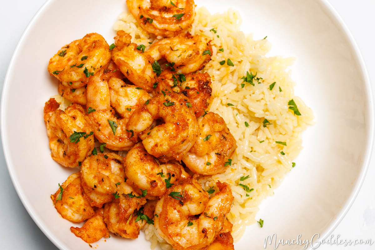 Shrimp on a bed of rice topped with fresh chopped parsley in an off-white bowl.