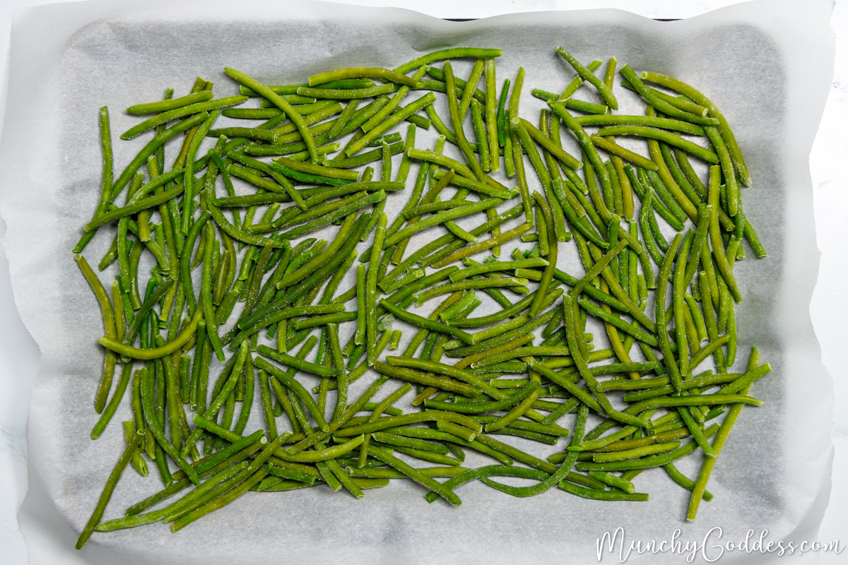 Frozen green beans spread out on a sheet pan lined with parchment paper.