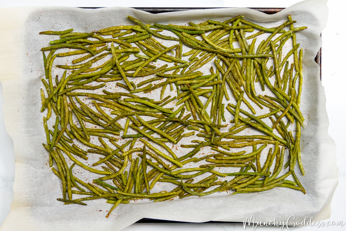 Roasted green beans on a sheet pan lined with parchment paper.