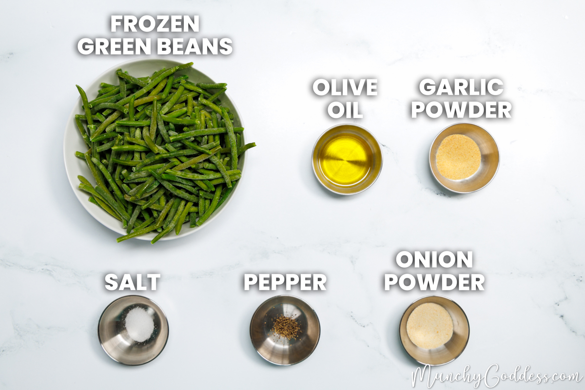 Roasted frozen green beans recipe ingredients in various dishes on a white marble surface: frozen green beans, olive oil, garlic powder, salt, ground black pepper, and onion powder.