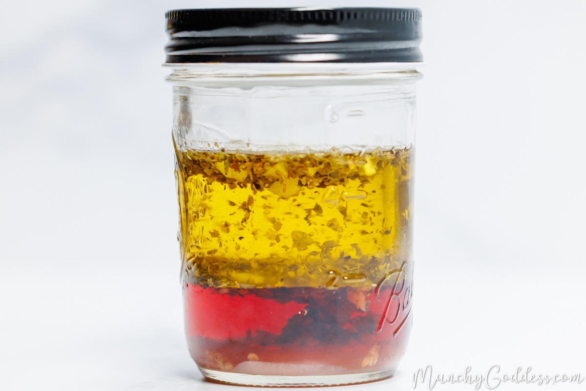 Olive oil, red wine vinegar, minced garlic, granulated sugar, salt, and ground black pepper unmixed in a mason jar with a black lid.