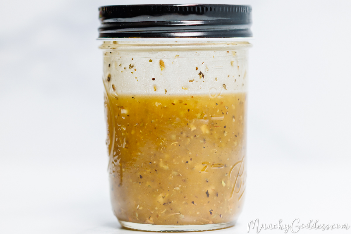 Olive oil, red wine vinegar, minced garlic, granulated sugar, salt, and ground black pepper shaken in a mason jar with a black lid until well blended to form a dressing.