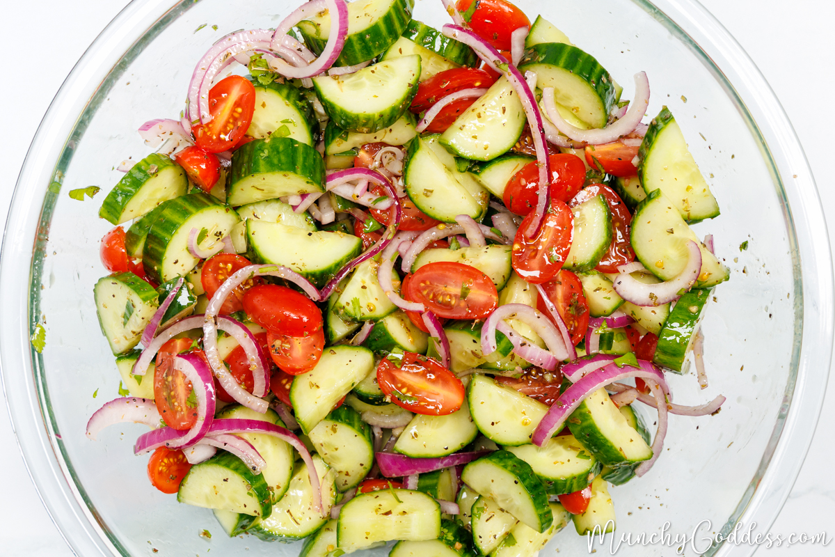 Cucumbers, cherry tomatoes, red onions and fresh parsley tossed in a homemade dressing in a large glass bowl.