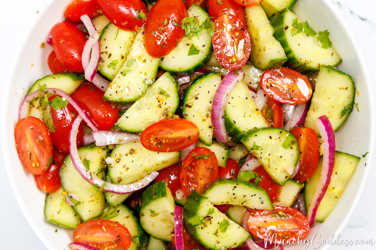 Cucumber tomato salad with red onions, fresh parsley, and homemade salad dressing in a white bowl.
